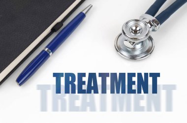 Tıp konsepti. Beyaz bir arka planda, bir not defteri ve steteskop, çift yazının yanında - TREATMENT