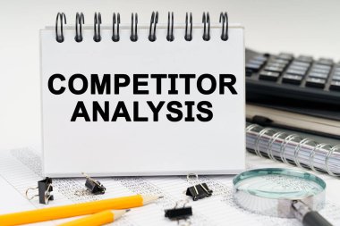 İş ve ekonomi kavramı. Masanın üzerinde bir büyüteç, kalemler, günlükler ve üzerinde COMPETITOR ANALYSIS yazan bir defter var.