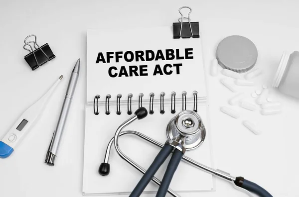 Medicine concept. On the table are a stethoscope, pills, a thermometer and a notebook with the inscription - affordable care act