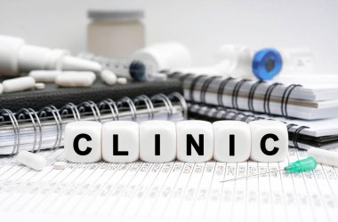 Tıp konsepti. Masanın üzerinde günlükler, ilaçlar ve üzerinde KLINIC yazan küpler var.