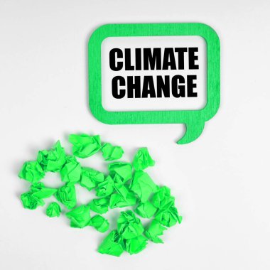 Ekoloji konsepti. Beyaz arka planda, yeşil buruşmuş kağıt parçaları ve içinde yazının olduğu bir tabela - İklim Değişikliği