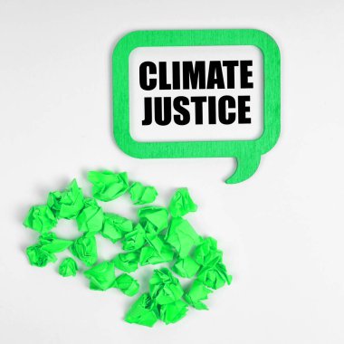 Ekoloji konsepti. Beyaz arka planda, buruşmuş yeşil kağıt parçaları ve içinde iklim adaleti yazan bir tabela.