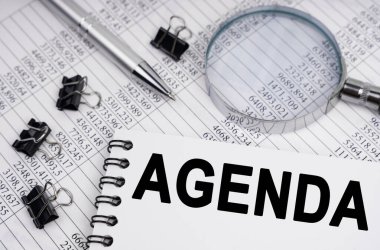 İş ve ekonomi kavramı. Masanın üzerinde bir büyüteç, raporlar, bir kalem ve üzerinde AGENDA yazan bir defter var.