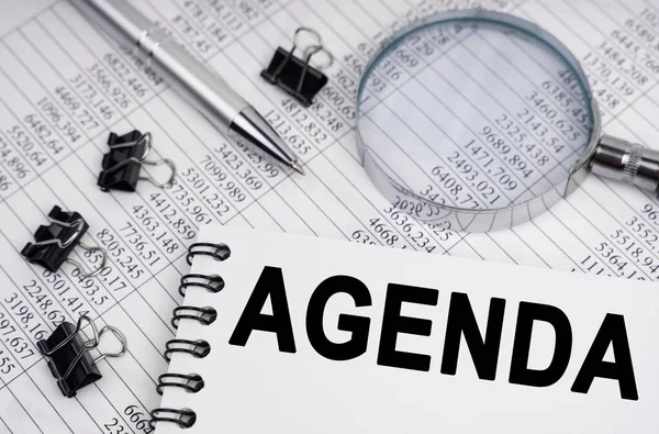İş ve ekonomi kavramı. Masanın üzerinde bir büyüteç, raporlar, bir kalem ve üzerinde AGENDA yazan bir defter var.