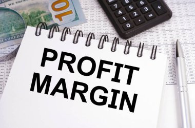 İş ve finans kavramı. Masanın üzerinde para, hesap makinesi ve içinde PROFIT MARGIN yazan bir defter var.