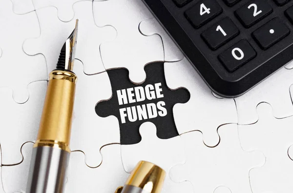 İş ve finans kavramı. Beyaz bulmacalarda bir hesap makinesi ve bir kalem var, açık bir hücrede bir yazı var - HEDGE FUNDS