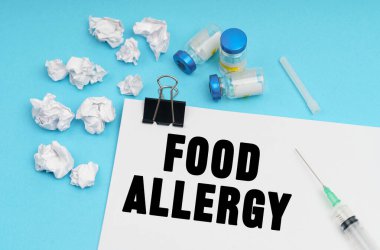 Tıp konsepti. Mavi arka planda, bir şırınga, ilaç, buruşmuş beyaz kağıt parçaları ve yazılı bir çarşaf - FOOD ALLERGY