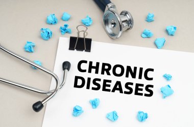Tıp konsepti. Masanın üzerinde bir stetoskop, bir kalem, buruşmuş mavi bir kağıt parçası ve üzerinde CHRONIC DISEASES yazan bir tabela var.