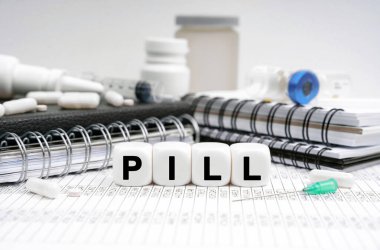 Tıp konsepti. Masanın üzerinde günlükler, ilaçlar ve üzerinde Pill yazan küpler var.