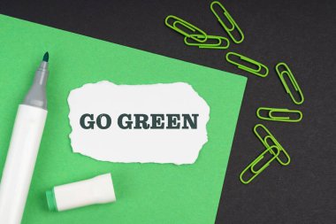 Ekoloji konsepti. Siyah bir arkaplanda, bir kalem, ataç, bir yaprak ve üzerinde yazı olan yırtık bir kağıt - GO GREEN