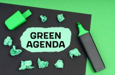 Ekoloji konsepti. Yeşil bir arkaplanda, bir işaret, siyah bir sayfa ve üzerinde yeşil gündem yazan yırtık bir kağıt.