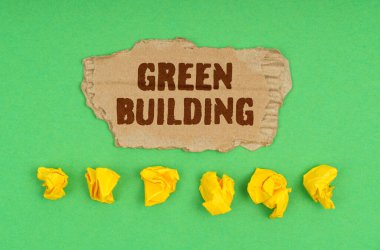 Ekoloji konsepti. Yeşil arka planda, buruşmuş sarı kağıt ve üzerinde yeşil bina yazan bir karton.