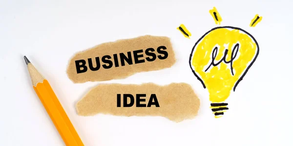 Business and finance concept. A lamp is drawn on a white sheet, there is a pencil and scraps of paper on which it is written - BUSINESS IDEA