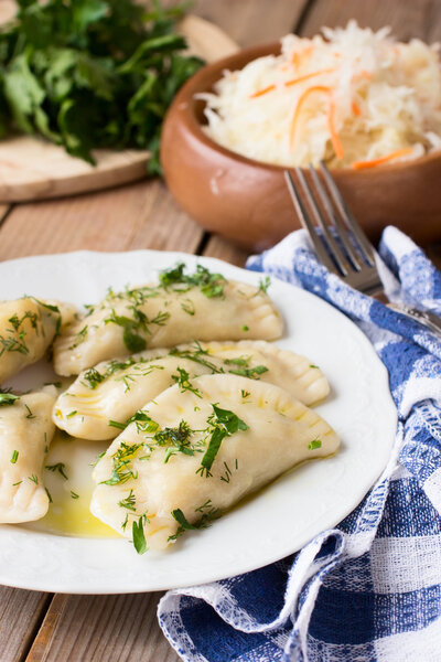 Traditional dish of Slavic cuisine. Potato-filled varenyky on a white plate on wooden table