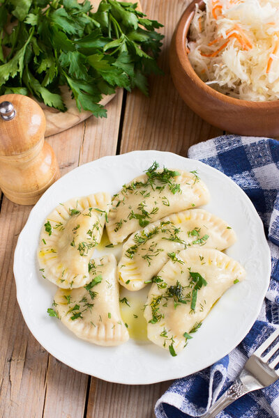 Traditional dish of Slavic cuisine. Potato-filled varenyky on a white plate on wooden table