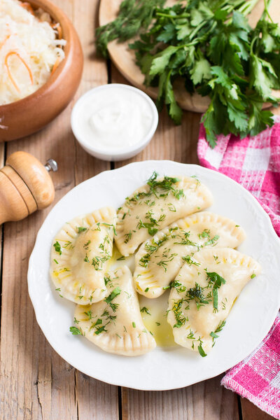 Traditional dish of Slavic cuisine. Potato-filled varenyky on a white plate on wooden table