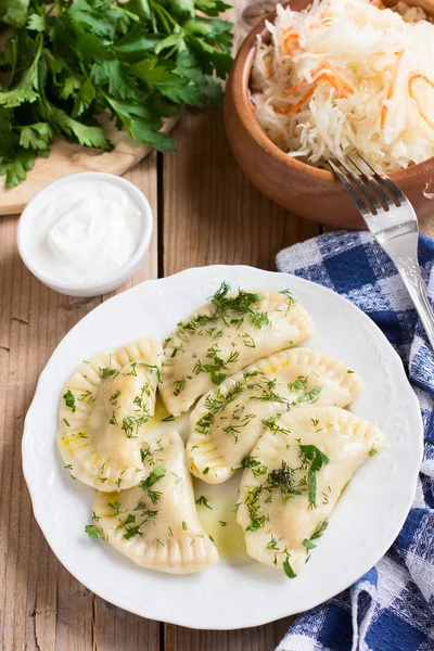 Piatto tradizionale della cucina slava. Varenyky ripieno di patate su un piatto bianco su tavolo di legno — Foto Stock