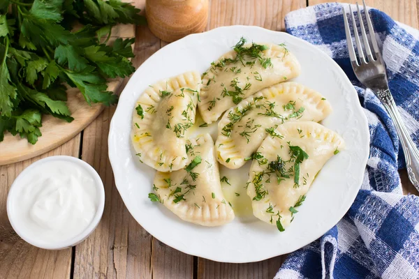 Piatto tradizionale della cucina slava. Varenyky ripieno di patate su un piatto bianco su tavolo di legno — Foto Stock