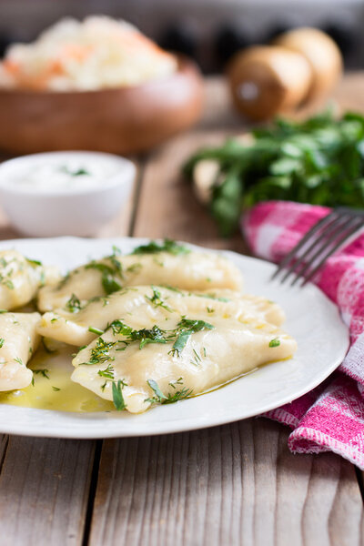 Traditional dish of Slavic cuisine. Potato-filled varenyky on a white plate on wooden table