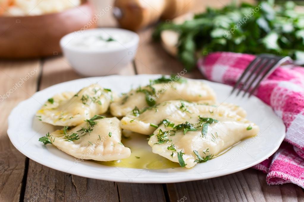 Traditional dish of Slavic cuisine. Potato-filled varenyky on a white plate on wooden table