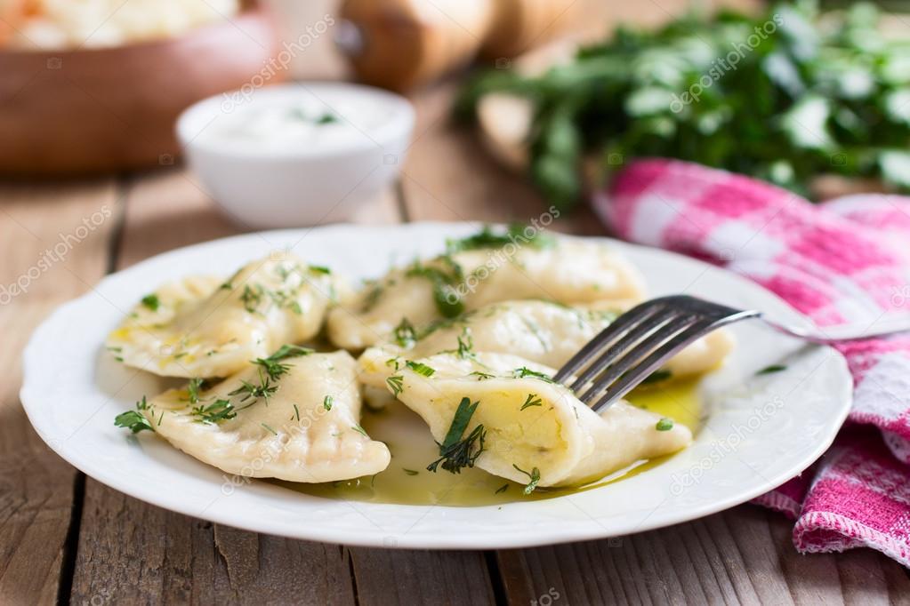 Traditional dish of Slavic cuisine. Potato-filled varenyky on a white plate on wooden table