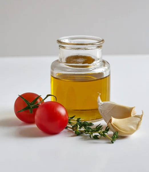 A jar of oil, two garlic cloves, tomatoes and a savory twig — Stock Photo, Image
