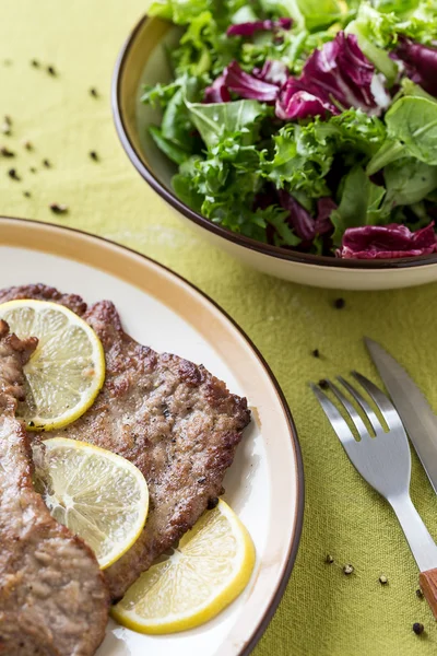 Fleischstücke mit Zitronenscheiben und grünem Salat — Stockfoto