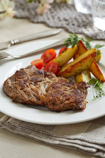 Ein Stück Schweinefleisch mit sautierten Kartoffeln und Tomaten — Stockfoto