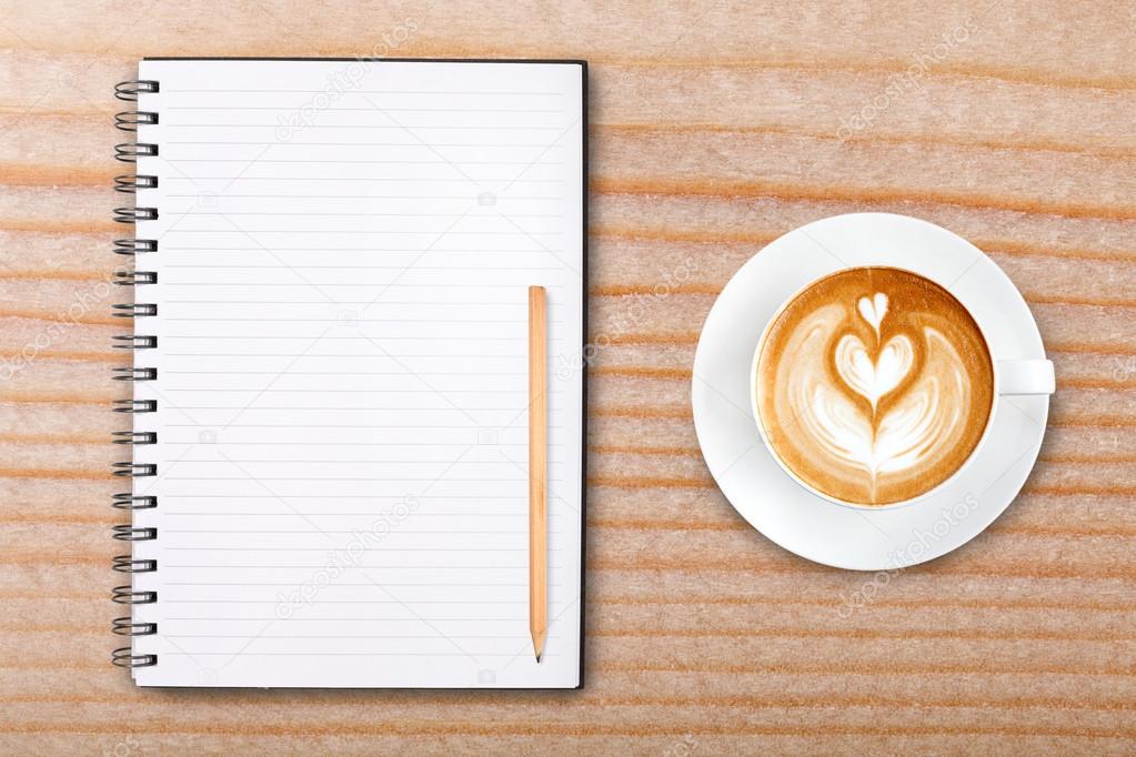 An open blank notebook with pencil and a cup of coffee on wooden