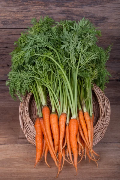 Bos van verse wortelen met groene bladeren op houten achtergrond — Stockfoto