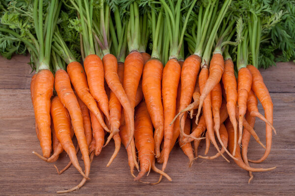 Bunch of fresh carrots with green leaves over wooden background