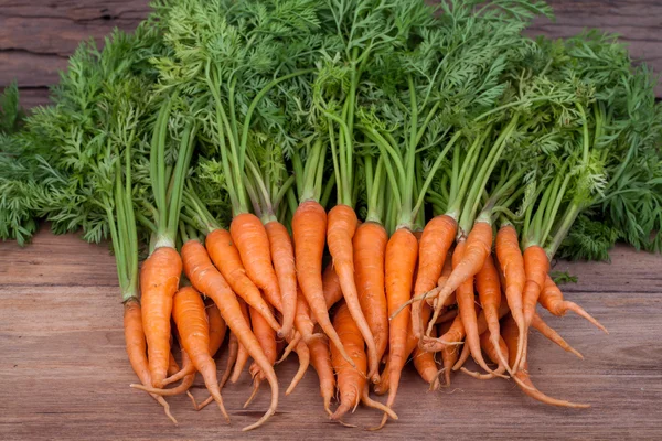 Manojo de zanahorias frescas con hojas verdes sobre fondo de madera — Foto de Stock