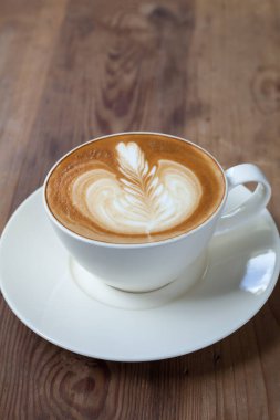 Ahşap sehpanın üzerine yakın plan latte sanat kahvesi.