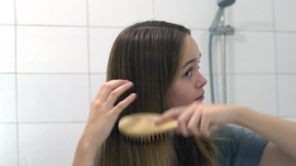 Attrayant jeune femme brossant les cheveux longs sains avec une brosse à cheveux en bois — Video