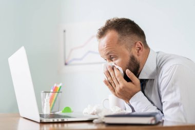 Ofiste çalışırken hapşıran, mendili olan hasta bir adam..