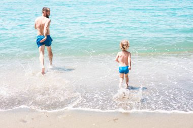 Baba ve oğul yaz tatilinde birlikte okyanusa doğru koşuyorlar. Yaz tatili, çocukluk hayatı, tatil seyahati.