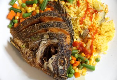 Kızarmış tilapia, sarı pirinç ve karışık sebzeli beyaz tabak.