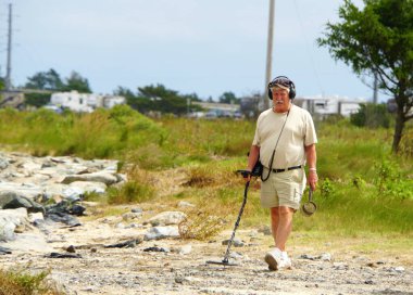 Bethany Beach, Delaware, ABD - 12 Eylül 2018 Indian River Inlet, Delaware yakınlarındaki kayıp eşyaları arayan metal dedektörlü yaşlı bir adam