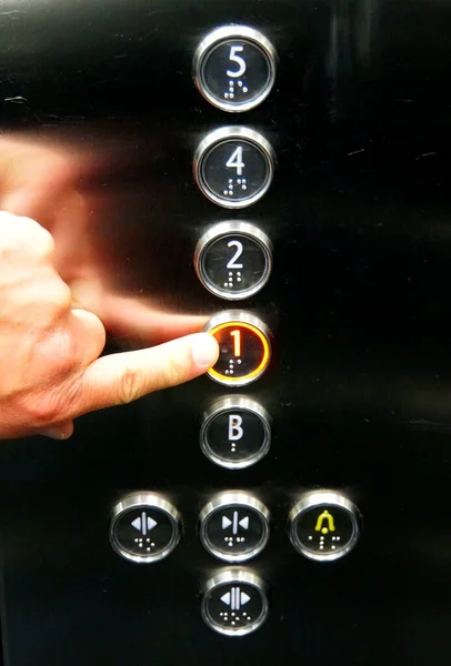 A finger touching the elevator buttons with Roman alphabet and Braille letters