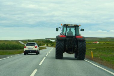 Reykjavik, İzlanda - 23 Haziran 2019 - Çevre yolunda büyük bir traktörün yanından geçen küçük bir araba