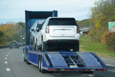 Kuzey New York, ABD - 18 Ekim 2025 - Mavi bir nakliye kamyonu Chevrolet Suburban SUV 'u da içeren iki araç taşıyor