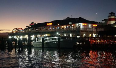 Madeira Sahili, Florida, ABD - 8 Kasım 2025 - Hooters restoranları, yerel mağazalar ve John 's Pass rıhtımına yanaşmış tekneler gece aydınlandı