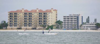 Madeira Sahili, Florida, ABD - 11 Kasım 2025 - Akdeniz ve modern stil binaları ile kıyı şeridi yakınında deniz kenarında bulutlu gökyüzü altında gezinen motorlu tekne.