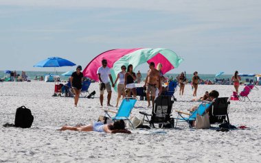Siesta Key Beach, Florida, ABD - 3 Ocak 2026 - Sahile gidenler dinlenirken, yürürken ve şemsiyelerin altında parçalı bulutlu bir günde renkli kumaş dalgaları