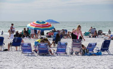 Siesta Key Beach, Florida, ABD - 3 Ocak 2026 - Sahile gidenler renkli şemsiyeler altında ve yoğun, geniş bir sahil şeridinde hafif dalgalarla çizgili şezlonglarda dinleniyorlar.