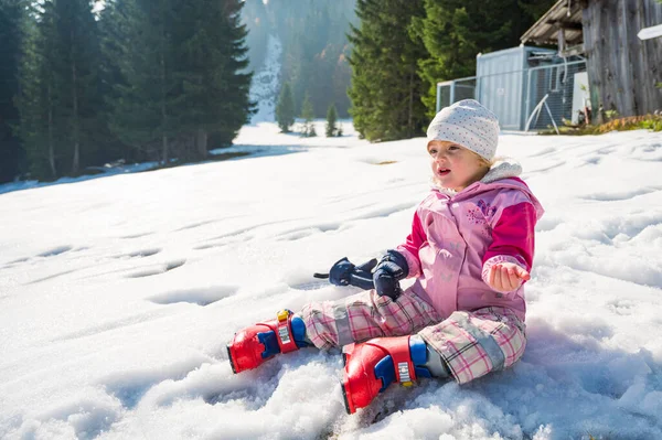 Cute girl sitting on snow wearing ski boots prepared to ride slopes. Royalty Free Stock Images