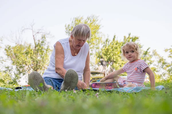 Бабушка с бабушкой небрежно сидит на одеяле, читает и разговаривает в парке.. — стоковое фото