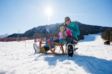 Kız ve anne bir kızakla yamaçta koşmaya hazırlanıyorlar..