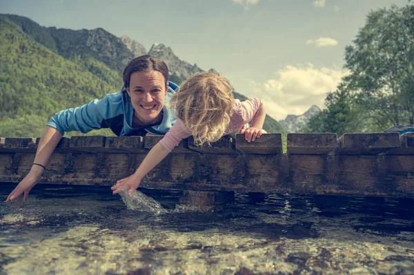 Matka a dcera leží na dřevěném mostě a dívají se do vody. — Stock fotografie