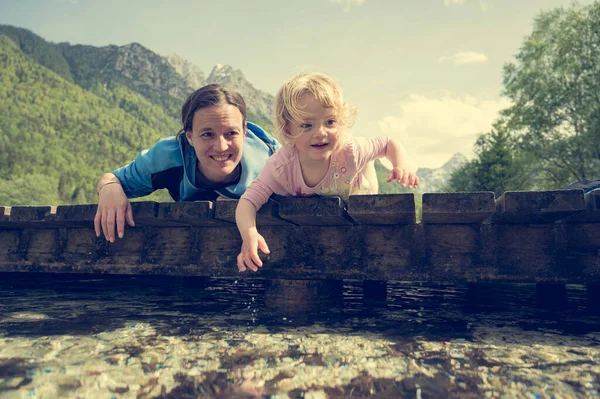 Mãe e filha deitada na ponte de madeira olhando para a água. — Fotografia de Stock